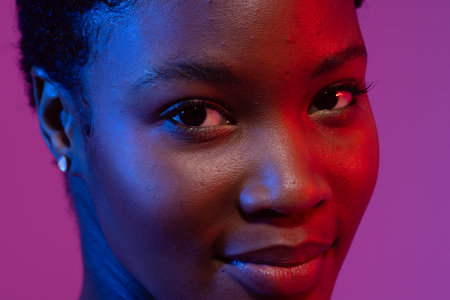 Close up of smiling african american woman with short hair in blue and red light. Femininity, face, facial expressions, body, skin, makeup, fashion and beauty, unaltered.の写真素材
