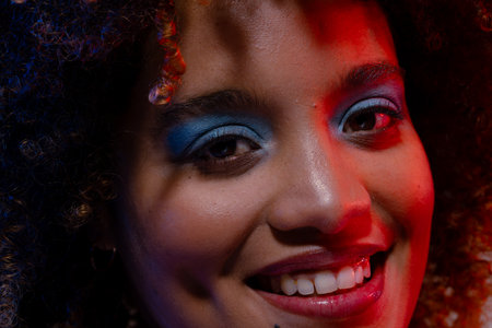 Close up of smiling biracial woman wearing blue eye shadow in red light. Femininity, face, facial...