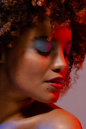 Biracial woman in blue eye shadow with eyes closed in red light. Femininity, face, facial expressions, body, skin and beauty, unaltered.の写真素材