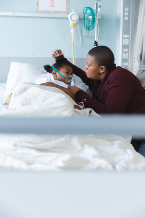 African american girl patient lying on bed with oxygen mask, with her mother at hospital. Hospital,...