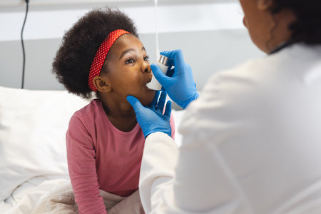 African american female doctor and girl patient using inhaler at hospital. Hospital, medicine and healthcare, unaltered.の写真素材