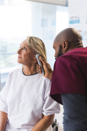 African american male doctor examining senior female caucasian patient using otoscopy. Hospital, work, medicine and healthcare, unaltered.の写真素材
