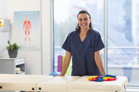 Portrait of happy female caucasian physiotherapist wearing scrubs at hospital. Hospital, physiotherapy, work, medicine and healthcare, unaltered.の写真素材