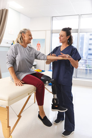 Caucasian female physiotherapist and senior woman with artificial leg massaging arm at hospital....