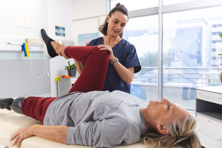 Caucasian female physiotherapist and senior woman with artificial leg stretching at hospital....