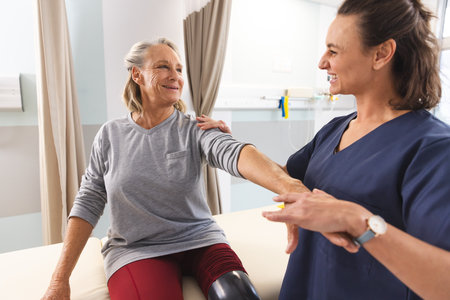 Caucasian female physiotherapist and senior woman with artificial leg massaging arm at hospital. Hospital, disability, physiotherapy, work, medicine and healthcare, unaltered.の写真素材