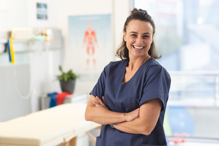 Portrait of happy female caucasian physiotherapist wearing scrubs at hospital. Hospital, physiotherapy, work, medicine and healthcare, unaltered.の写真素材