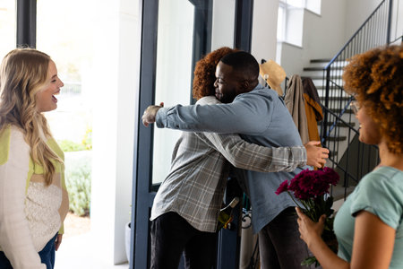 Happy diverse group of friends welcoming and embracing at home with flowers and bottle of wine. Domestic life, friendship and lifestyle, unaltered.の写真素材