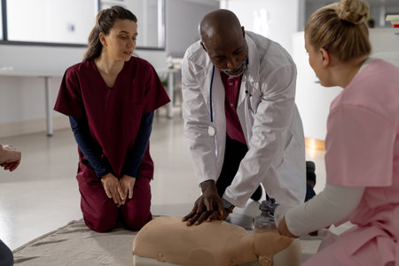 Senior african american male doctor with diverse trainee doctors learning cpr on model at hospital. Hospital, traineeship, medicine, healthcare and work, unaltered.の写真素材