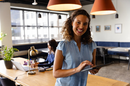 Portrait of happy caucasian casual businesswoman using tablet in office. Casual office, business, professional, communication and work, unaltered.の写真素材