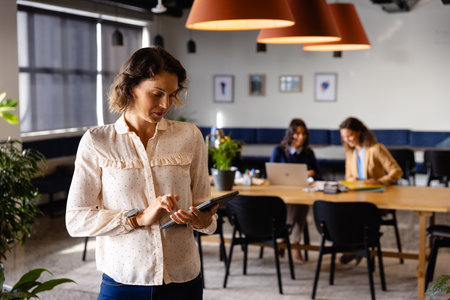 Caucasian casual businesswoman using tablet in office. Casual office, business, lifestyle, communication and work, unaltered.の写真素材