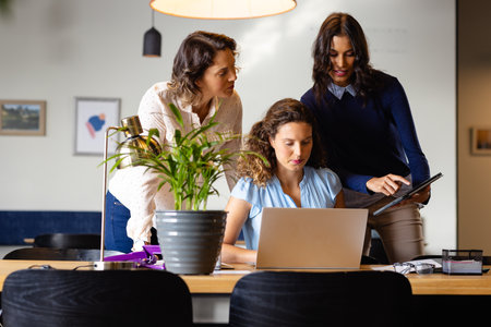 Diverse casual businesswomen discussing using laptop and tablet in office. Casual office, business, professional, communication, teamwork and work, unaltered.の写真素材