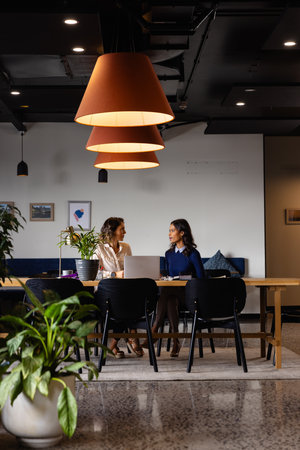 Diverse female colleagues in discussion using laptop in casual office meeting. Casual office, teamwork, business, lifestyle, communication and work, unaltered.の写真素材