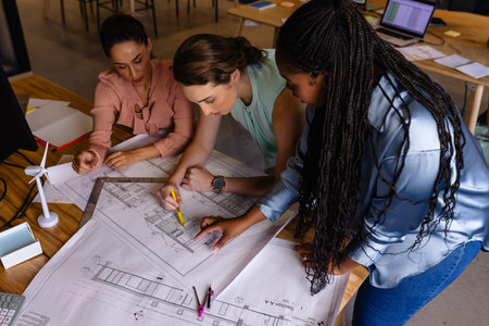 Diverse female architects in discussion using blueprints in casual office meeting. Casual office,...