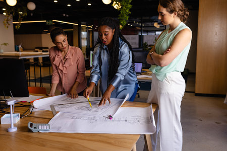 Diverse female architects in discussion using blueprints in casual office meeting. Casual office, teamwork, business, lifestyle, creative work, design and work, unaltered.の写真素材
