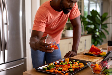 African american man preparing meal using tablet in kitchen. Lifestyle, food, cooking, healthy lifestyle, communication, recipe and domestic life, unaltered.の写真素材