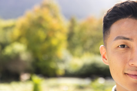 Half portrait of happy asian man smiling in sunny garden, copy space. Wellbeing, summer, free time,...
