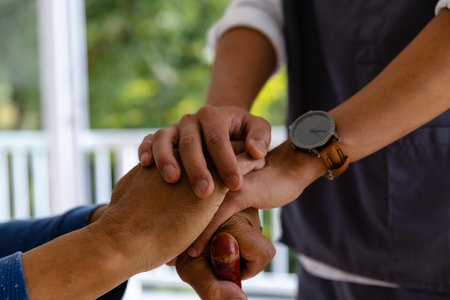 Hands of diverse male doctor and senior male patient holding walking stick at home. Medical services, check up, home visit, healthcare, wellbeing and senior lifestyle, unaltered.の写真素材