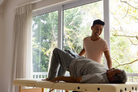 Happy diverse male physiotherapist advising and senior male patient exercising. Physiotherapy, healthcare, wellbeing and senior lifestyle, unaltered.の写真素材