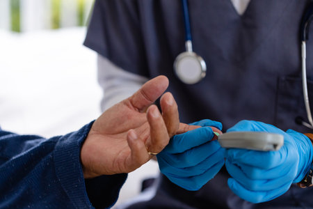 Hands of diverse male doctor testing blood of senior male patient at home. Medical services, check up, home visit, healthcare, wellbeing and senior lifestyle, unaltered.の写真素材