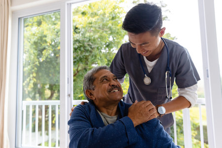 Happy diverse male doctor discussing with senior male patient in wheelchair at home. Medical services, check up, home visit, healthcare, wellbeing and senior lifestyle, unaltered.の写真素材