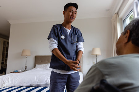 Diverse male doctor discussing with senior male patient in wheelchair at home. Medical services, check up, home visit, healthcare, wellbeing and senior lifestyle, unaltered.の写真素材