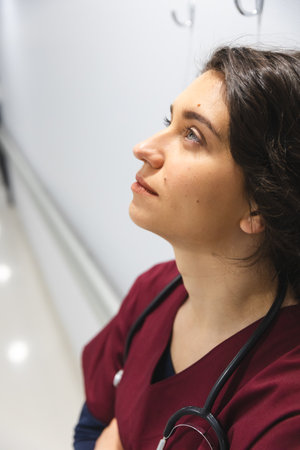 Tired caucasian female doctor wearing scrubs, leaning on wall in corridor at hospital. Hospital, mental health, medicine, healthcare and work, unaltered.の写真素材