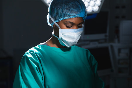 African american female surgeon wearing surgical gown and face mask in operating theatre. Hospital, surgery, medicine, healthcare and work, unaltered.の写真素材