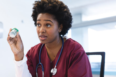 African american female doctor wearing scrubs and stethoscope, having video call at hospital. Hospital, communication, video call, medicine, healthcare and work, unaltered.の写真素材