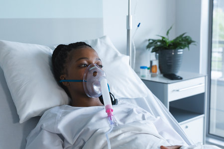 African american female patient with oxygen mask, lying on bed in hospital room. Hospital, medicine...