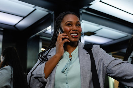 Happy plus size african american casual businesswoman talking on smartphone in elevator. Casual office, communication, business, professional and work, unaltered.の写真素材