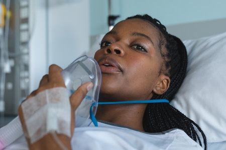 African american female patient with oxygen mask, lying on bed in hospital room. Hospital, medicine...
