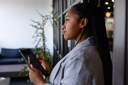 Plus size african american casual businesswoman using tablet in office window. Casual office, business, professional, communication and work, unaltered.の写真素材