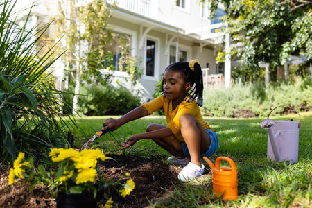 African american girl digging dirt with tool on grassy land in yard outside house. Unaltered, lifestyle, gardening, nature and childhood concept.の写真素材