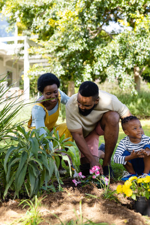 African american parents with son planting fresh flowers on field against trees in backyard. Unaltered, lifestyle, gardening, family, love, togetherness, weekend, nature and childhood concept.の写真素材