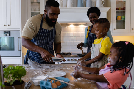 African american children playing with flour while parents making pancakes in kitchen. Unaltered, lifestyle, family, love, togetherness, childhood, food, preparation and learning concept.の写真素材