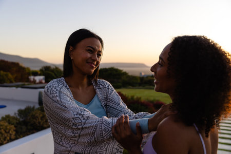 Biracial lesbian couple embracing in garden at sunset. Lifestyle, relationship, togetherness, nature and domestic life, unaltered.の写真素材