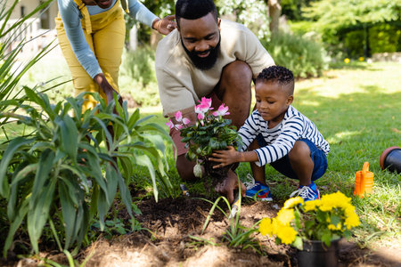 African american woman standing by father and son planting fresh flowers in field at yard. Unaltered, lifestyle, gardening, family, love, togetherness, nature and childhood concept.の写真素材