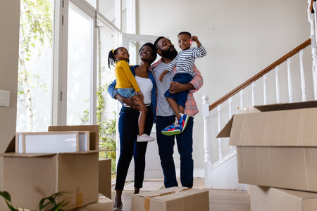 Happy african american parents carrying children with key by cardboard boxes in new home, copy...