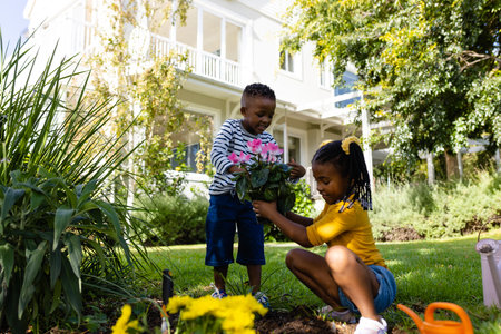 African american boy giving fresh flowers to sister planting in yard outside house. Unaltered, lifestyle, gardening, family, love, togetherness, nature and childhood concept.の写真素材