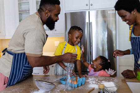 Playful african american parents and children applying flour on each others faces in kitchen. Unaltered, lifestyle, family, love, togetherness, childhood, food, preparation and learning concept.の写真素材