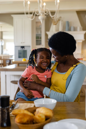 African american mother sitting with cheerful daughter at dining table at home. Unaltered, lifestyle, family, love, togetherness, childhood, croissant, breakfast, morning, home concept.の写真素材