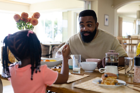 African american father talking with daughter while having breakfast at dining table at home. Unaltered, lifestyle, family, love, togetherness, childhood, morning, food and home concept.の写真素材