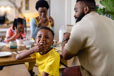 African american boy laughing while having breakfast with family at dining table at home. Unaltered, lifestyle, family, love, togetherness, food, childhood, morning and home concept.の写真素材
