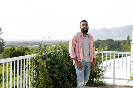 Portrait of happy african american man staying on sunny terrace with copy space. Lifestyle, nature and domestic life, unaltered.の写真素材