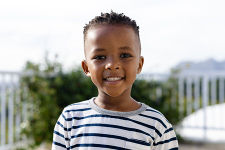 Portrait of cute african american boy smiling at camera while standing against clear sky in yard. Copy space, unaltered, childhood, face, happy and lifestyle concept.の写真素材