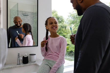Happy biracial father and daughter brushing teeth together in bathroom in the morning. Family, togetherness, self care, hygiene, healthy living and domestic life, unaltered.の写真素材