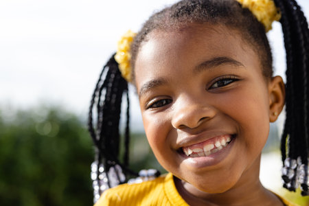 Close-up portrait of cute african american girl smiling at camera against clear sky in yard. Unaltered, childhood, face, happy and lifestyle concept.の写真素材