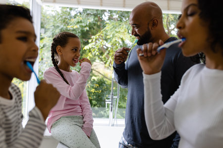 Happy biracial parents, son and daughter brushing teeth together in bathroom in the morning. Family, togetherness, self care, hygiene, healthy living and domestic life, unaltered.の写真素材