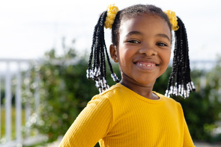 Portrait of happy african american girl staying on sunny terrace. Lifestyle, nature, childhood and domestic life, unaltered.の写真素材